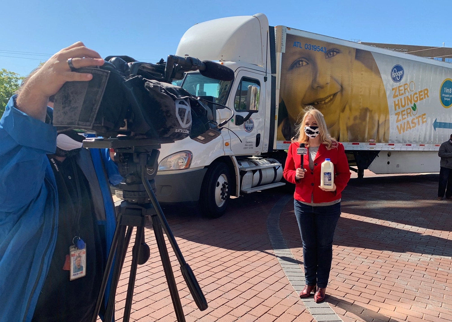 amanda lucey in front of a Kroger semi truck with a microphone and a half gallon of milk being videotaped MOMM