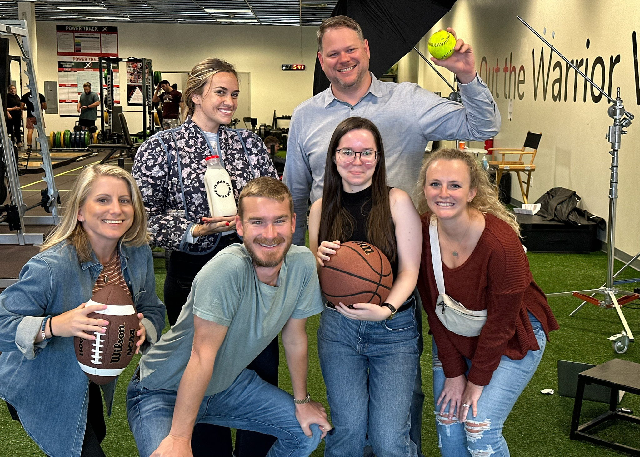 six TPI staff members pose with various sports balls and milk at the end of a video shoot